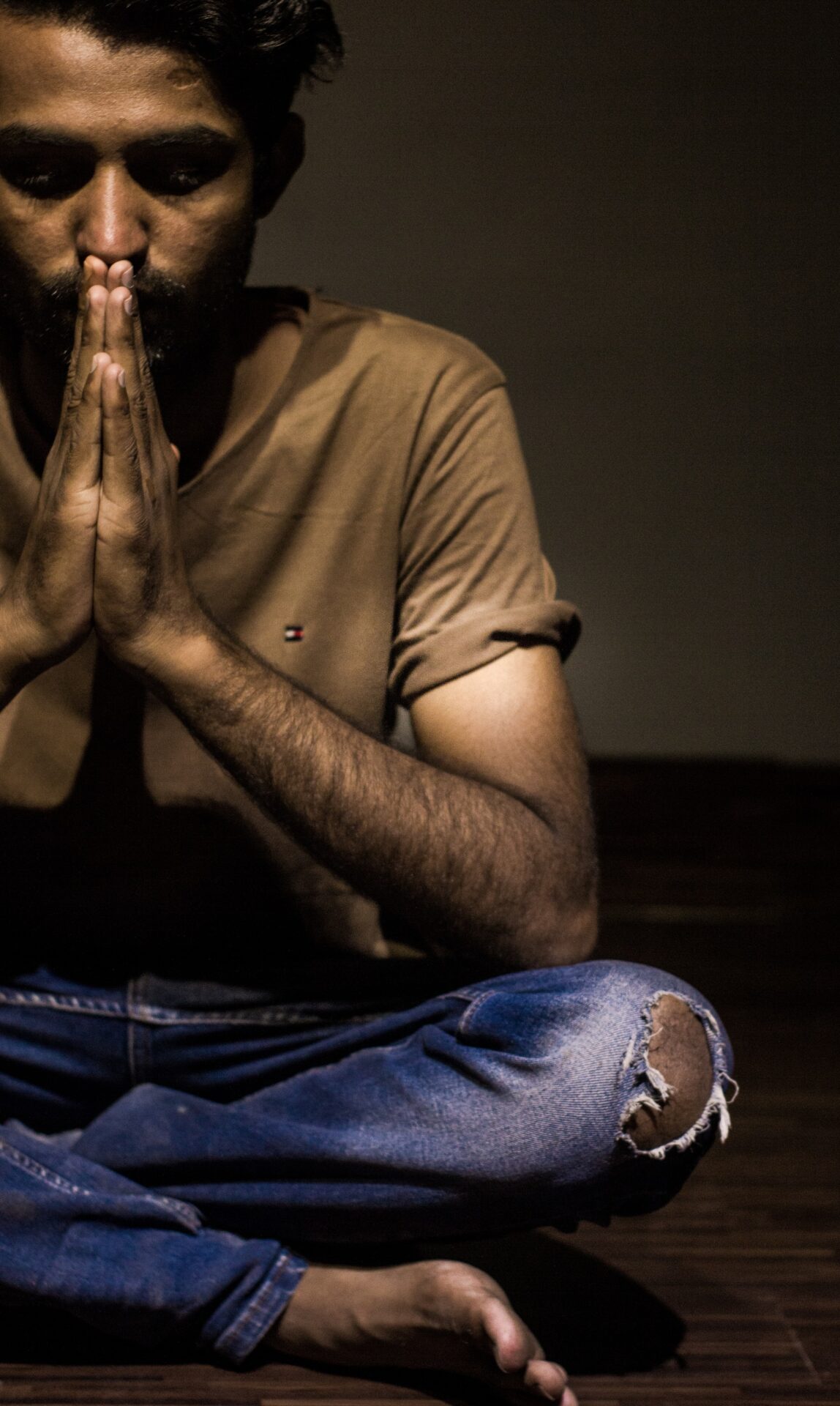 man wearing beige crew-neck shirt and blue faded jeans meditating