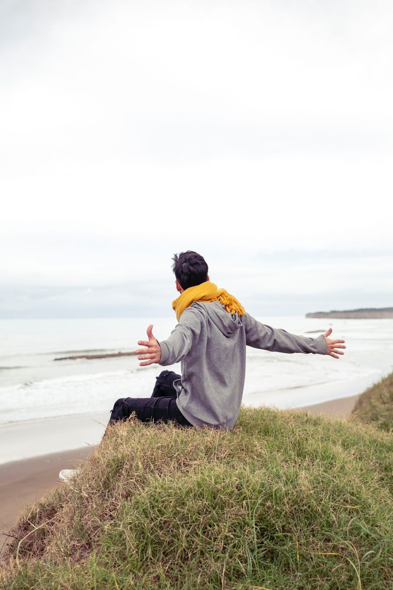 man open wide arms while sitting on grass