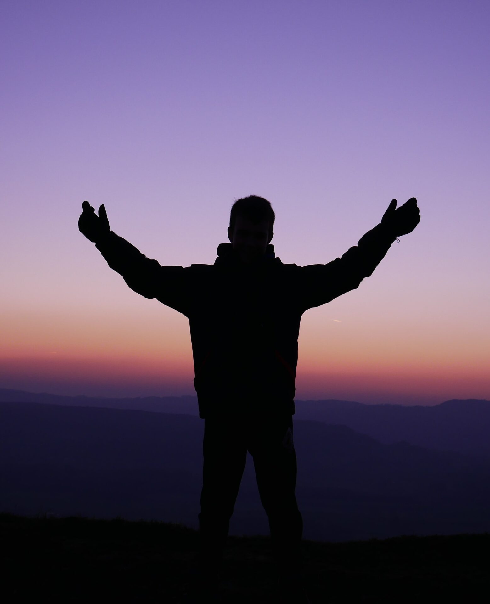 silhouette of man raising his hands during sunset