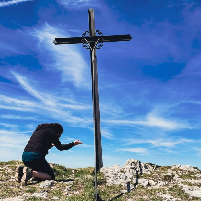 a man kneeling down next to a cross on top of a hill