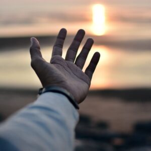 a hand reaching out towards the ocean at sunset