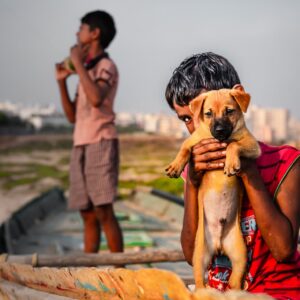 boy in red sleeveless shirt holding brown short-coated puppy