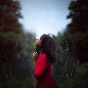 woman wearing red sweatshirt looking at top between trees near grass during daytime