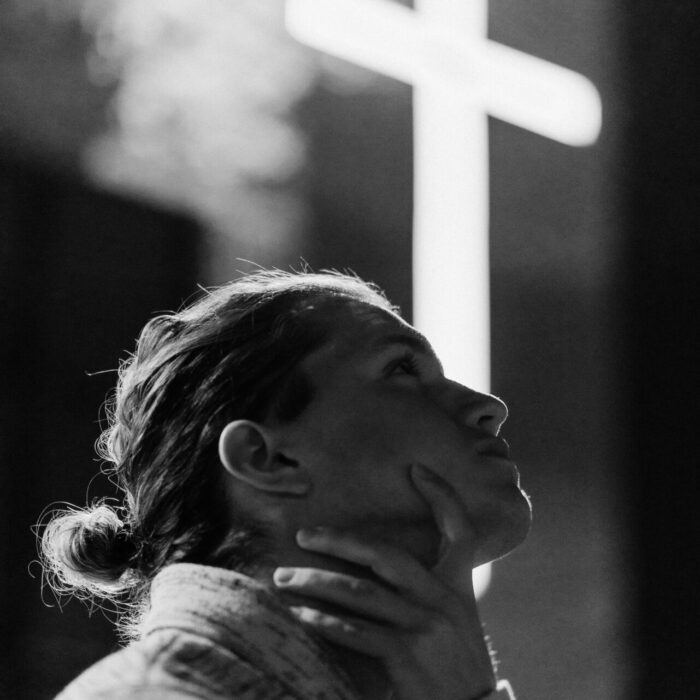 grayscale photography of woman standing near white cross signage