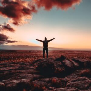 person standing on rock raising both hands