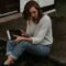 woman carrying book sitting on brown concrete pathway