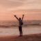 man in white shirt and black shorts standing on seashore during sunset