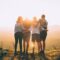 four person hands wrap around shoulders while looking at sunset