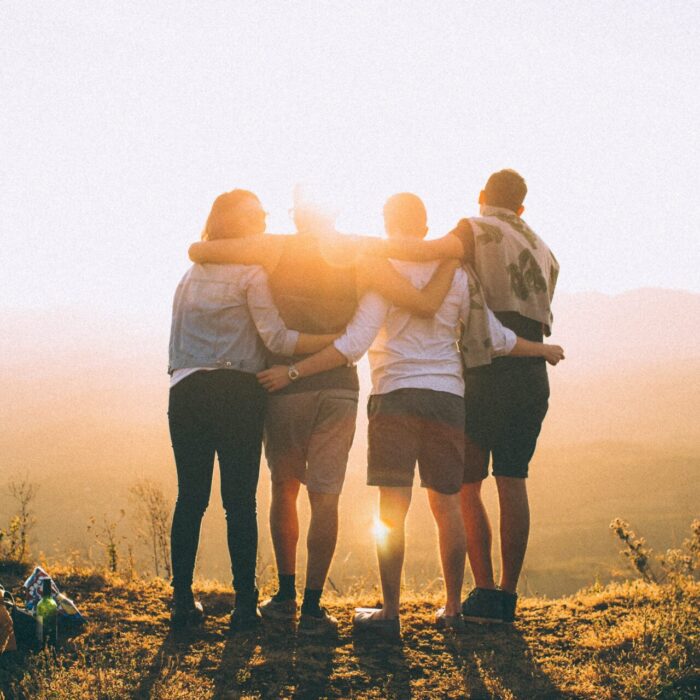 four person hands wrap around shoulders while looking at sunset