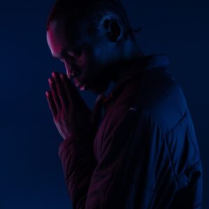 man wearing black bubble jacket with praying hands standing while facing his right side