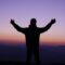 silhouette of man raising his hands during sunset