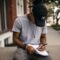 person in black adidas cap sitting on bench writing on notebook