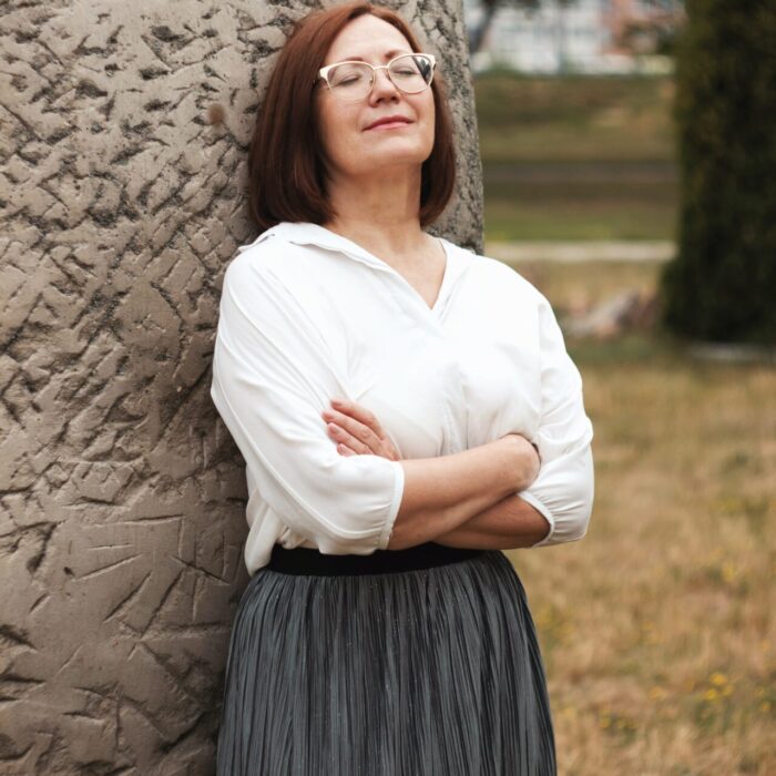 woman in white long sleeve shirt and black skirt standing beside brown tree during daytime